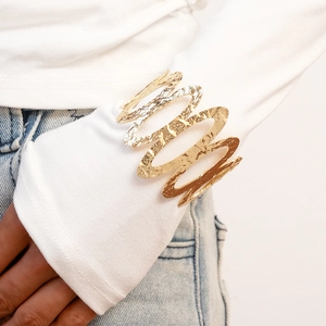 Detailed view of wide gold irregular metal cuff with hammered texture on white sleeve