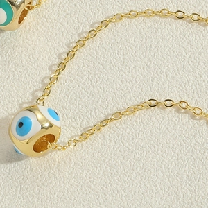 Macro shot of gold-plated evil eye necklace with blue enamel charm on textured background