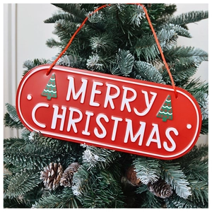 Macro detail of red metal Merry Christmas sign hanging on a green tree with pine cones