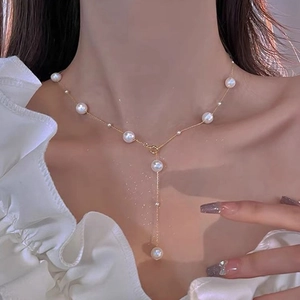 Nahaufnahme einer eleganten Y-Halskette aus Gold mit weißen Perlen am Model getragen