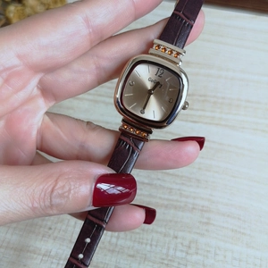 Detail of square gold quartz watch with Roman numerals and brown leather strap on wrist