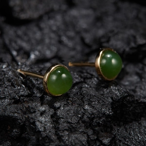 Macro shot of green chalcedony stud earrings with gold finish on a textured black stone