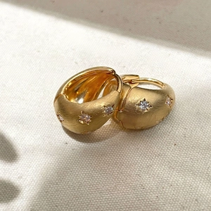 Macro view of gold star earrings with cubic zirconia and brushed metal texture