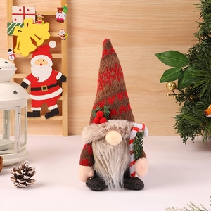 Close-up of Christmas gnome with knitted snowflake hat holding a red candy cane