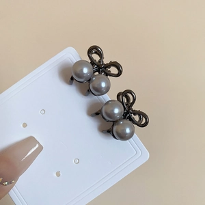 Close-up of small dark grey metal bow hair clips with pearls on a display card