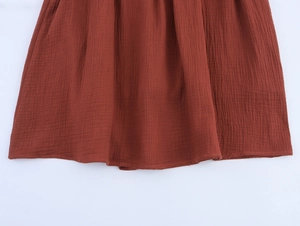 Detailed close-up of reddish-brown linen fabric texture and hem stitching on summer dress