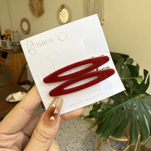 Paire de barrettes à cheveux rouge foncé brillant sur carte blanche tenue à la main