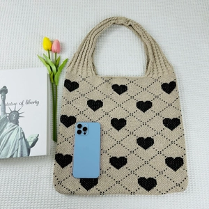 Flat lay of a beige knitted tote bag with black heart patterns and lifestyle props