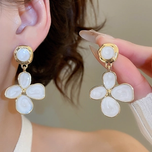 Détail de boucles d'oreilles fleurs en émail blanc bordées d'or sur mannequin