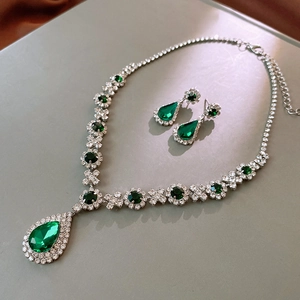 Macro shot of silver jewelry set with teardrop emerald pendants and shining crystals