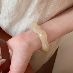 Detail of acrylic wavy bangle with cream marble texture worn on model's wrist