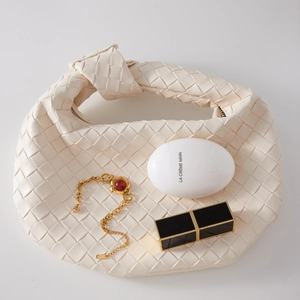 Detail of white woven leather handbag with knot handle and golden metal chain bracelet