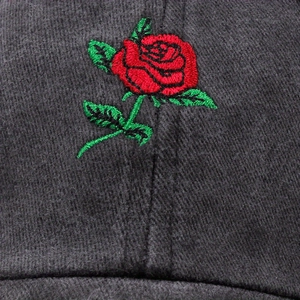 Dettaglio del ricamo rosa rossa su un cappellino in cotone nero con trama del tessuto