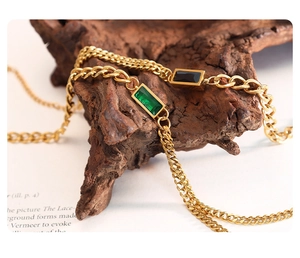 Detail of gold double-layer chain bracelet with emerald and black rectangle zircons