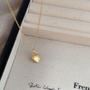 Polished gold heart necklace with zircon and 'for me' engraving on a beige background