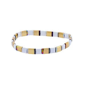 Detail of bohemian stretch bracelet with white and gold enamel square beads on white background