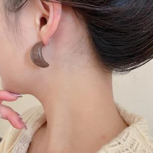 Detail of mocha brown acrylic C-shaped earrings worn with a cream knit sweater