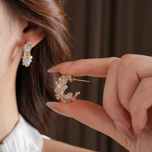 Macro detail of C-shaped gold earrings with light blue stones and small white pearls