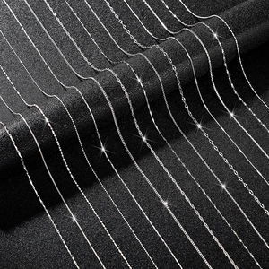 Macro shot of assorted silver box, snake, and twisted chains on a textured black background