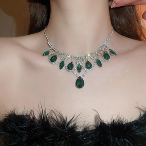 Close-up of elegant silver necklace with green pear-cut gems and diamonds on a model