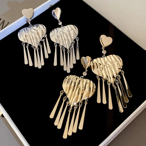 Detail of gold and silver heart tassel earrings with pleated metal texture on black velvet