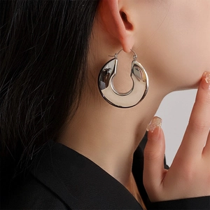 Macro shot of large polished silver U-shaped hoop earrings on a model in a dark setting