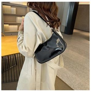 Detailed view of the glossy black patent leather baguette shoulder bag worn by a model