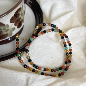Detailed view of colorful 2mm beaded necklace with gold clasp on white linen fabric