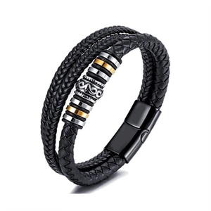 Detail of multi-layer braided black leather bracelet with gold and silver metal charms