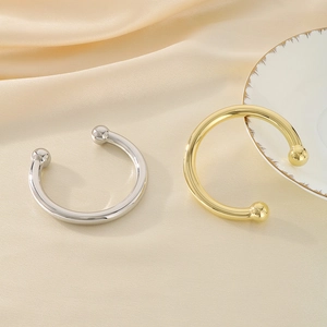 Detail of C-shaped open bangles in gold and silver finish with ball ends on silk