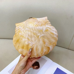 Detail of a shell-shaped amber evening clutch bag with golden metal clasp and marble pattern