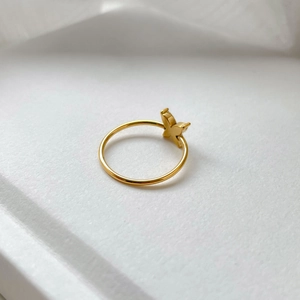 Detailed top view of a slim gold butterfly ring with zircon on a textured white surface