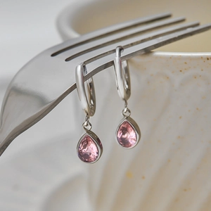 Silver hoop earrings with pink teardrop crystal hung on a silver fork backdrop