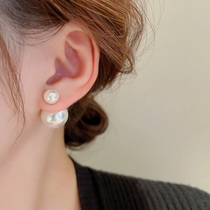 Detailed view of silver needle double-sided pearl earrings worn on a female ear