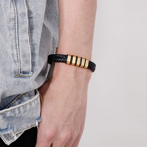 Gros plan d'un bracelet en cuir tressé noir pour homme avec accents d'anneaux dorés