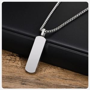 Macro detail of a blank silver rectangle pendant with a box chain on a dark textured box