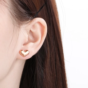 Boucles d'oreilles cœur dorées 18 carats portées par un mannequin sur fond blanc