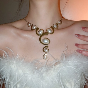 Detail of golden spiral necklace with white pearls worn by a model in feather top