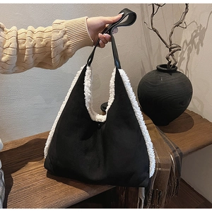 Detail of contrast tote bag with black suede texture and white faux fur trim on wooden bench