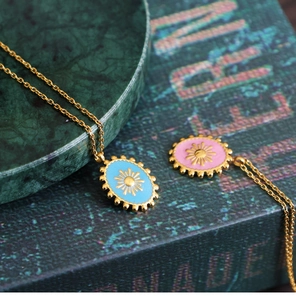 Close-up of starburst enamel oval pendants on gold chains with marble background