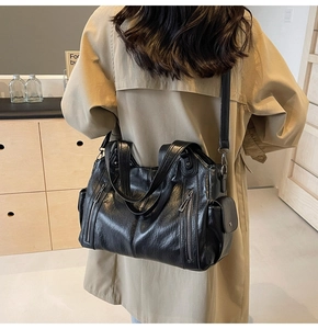Detail of black faux leather tote bag with side pocket shown on khaki trench coat