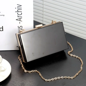 Elegant black acrylic evening clutch bag with gold chain and mirror finish on dark wood table