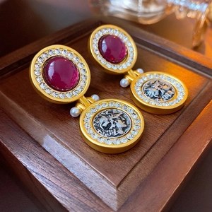 Vintage gold earrings with red stones, rhinestones, coin charms, and pearls on a wood tray