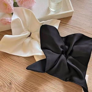 Detail of elegant black and white silk satin scrunchies on a wooden table with floral decor