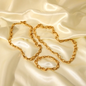 Close-up of gold geometric chain link necklace and bracelet set on beige silk fabric