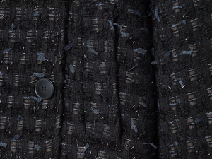 Close-up of black tweed fabric with metallic silver threads and a matte round button