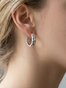 Detail of silver C-shaped earrings with irregular hammered texture on model's ear