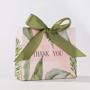 Detailed view of a pink wedding favor box with green leaf patterns and olive ribbon bow