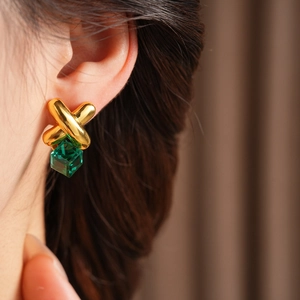 Close-up of vintage gold cross earrings with a green cube crystal pendant on model