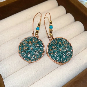 Detail of bohemian bronze hollow disk earrings with blue beads on cream velvet display